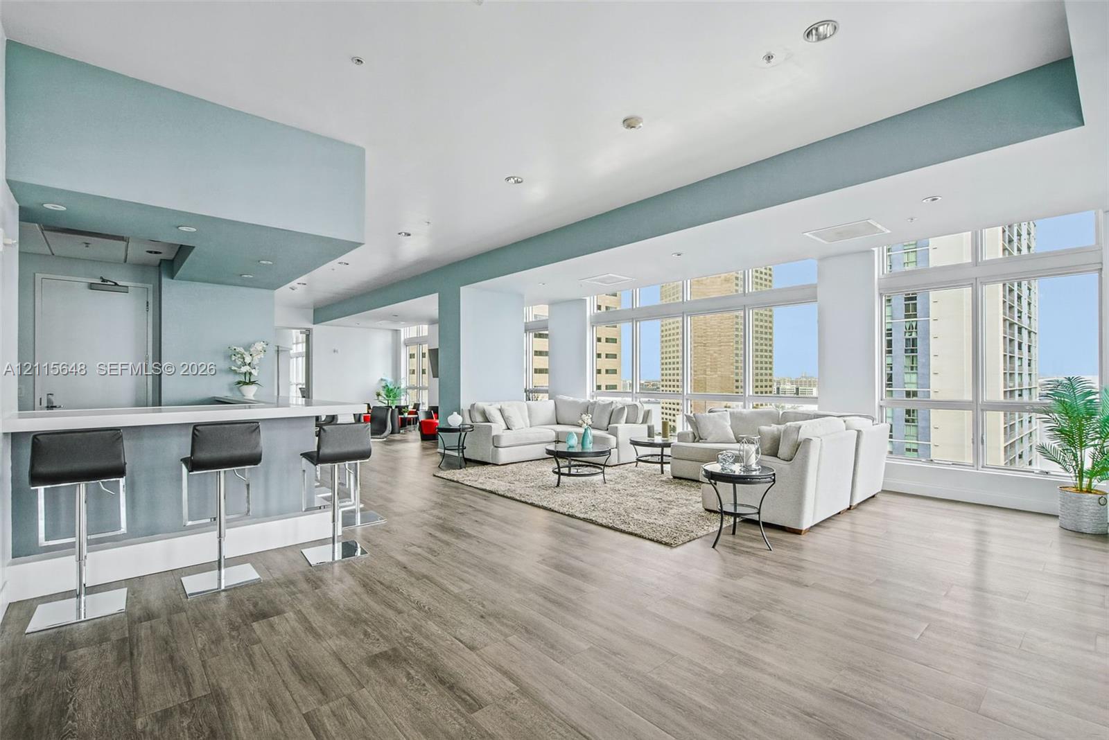 Open-concept floor plan featuring expansive floor-to-ceiling windows, wood-finish flooring, recessed lighting, and a built-in wet bar with a stone-top counter