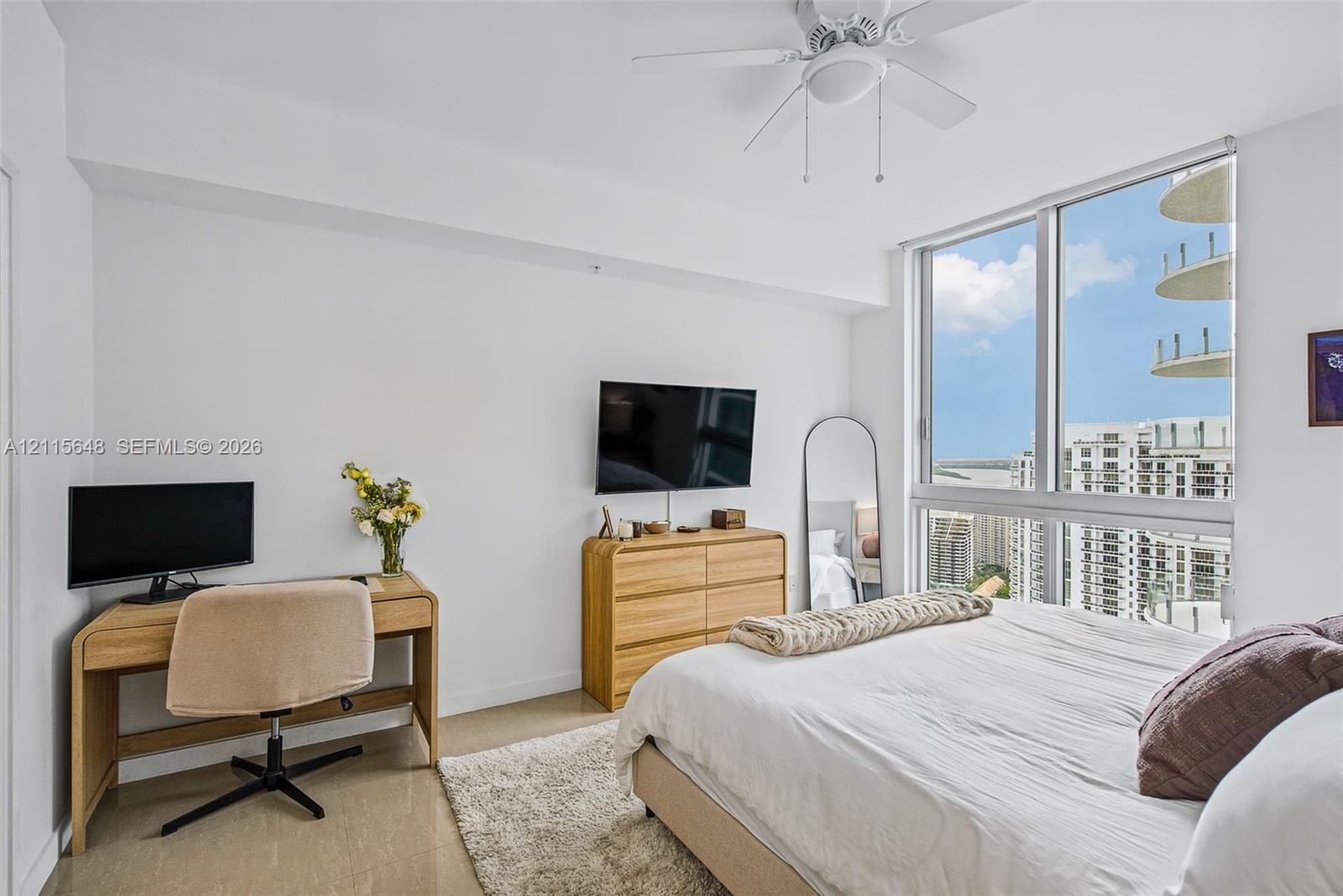 Floor-to-ceiling windows, neutral hard-surface flooring, and a ceiling-mounted fan