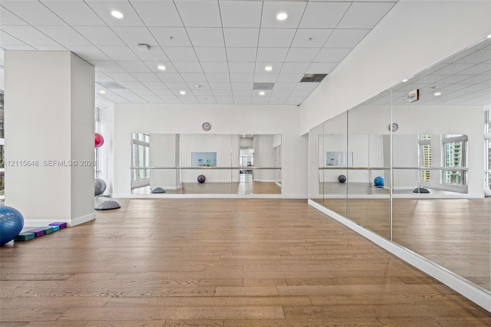 Studio space featuring wood-finish flooring, full-length wall mirrors, a metal ballet barre, recessed ceiling lighting, and a drop ceiling