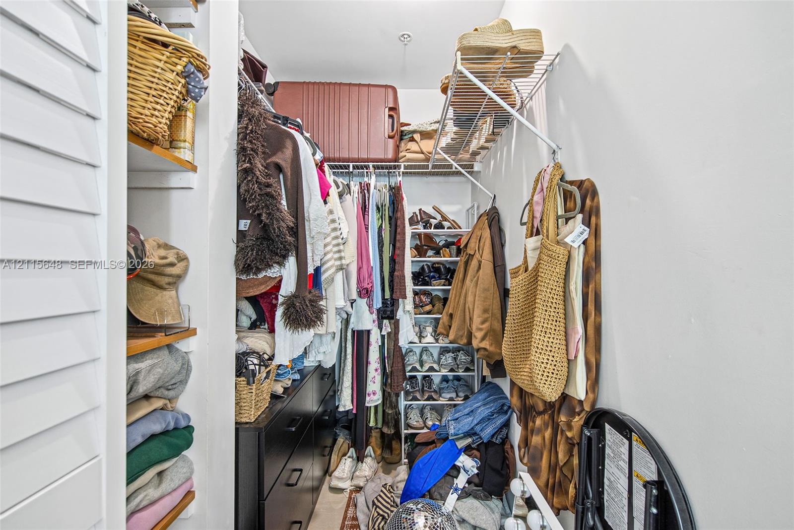 Walk-in closet featuring multi-tiered wire shelving, integrated wood-finish shelving units, and a shutter-style door