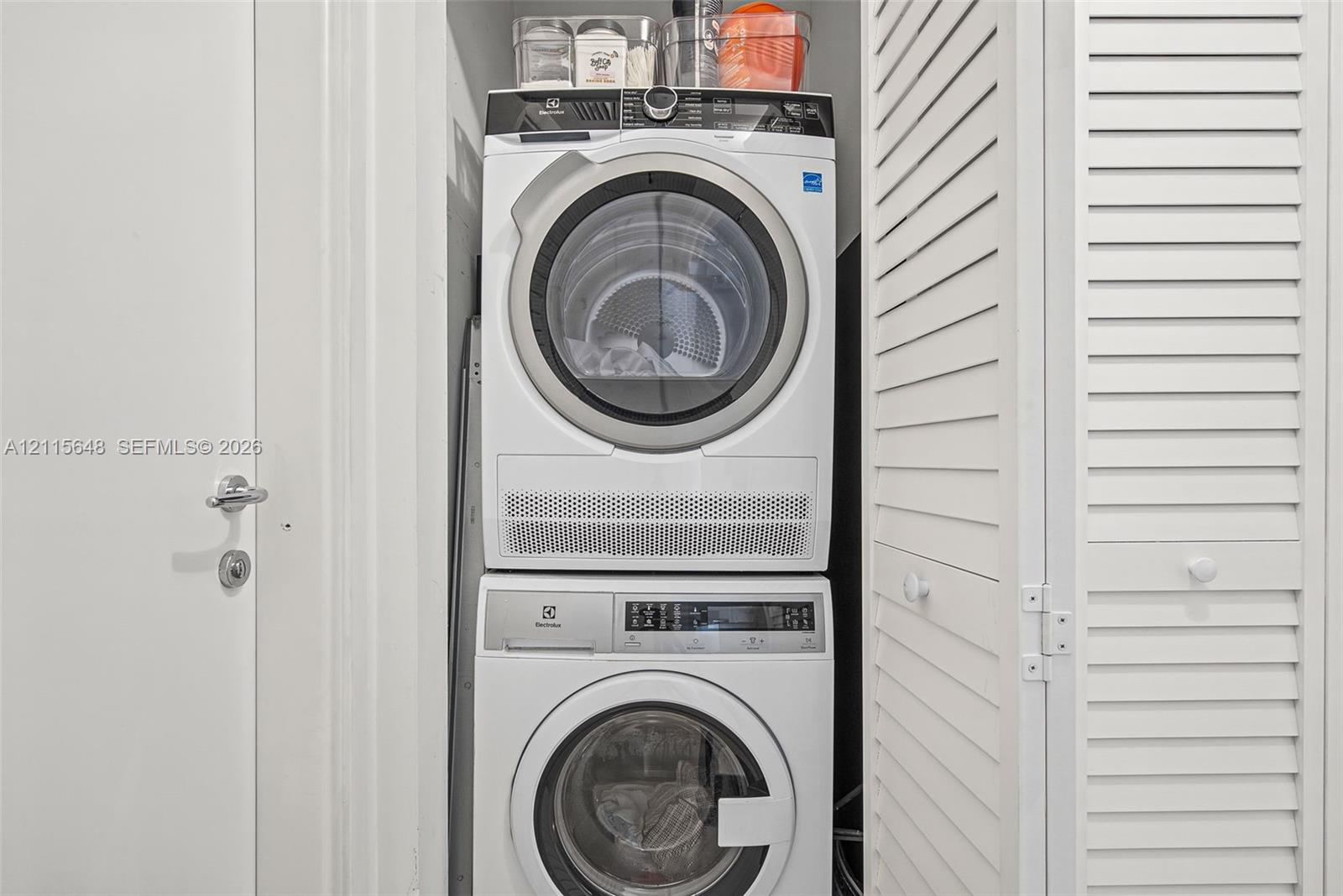 Stacked Electrolux front-load washer and dryer unit enclosed by white louvered doors