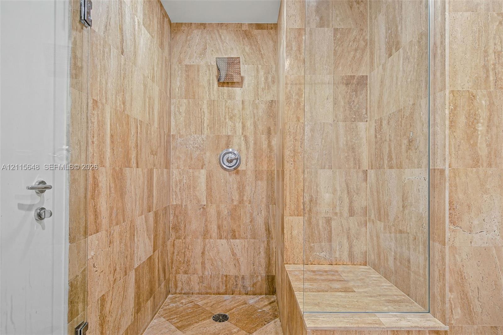 Walk-in shower featuring floor-to-ceiling stone tile, a built-in tiled bench, a glass enclosure, and a circular wall-mounted shower fixture