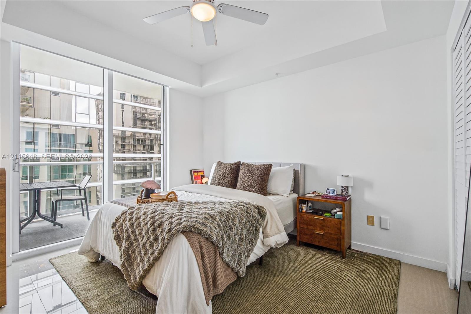 Floor-to-ceiling glass sliding doors, tray ceiling, ceiling fan with integrated light, and louvered closet doors
