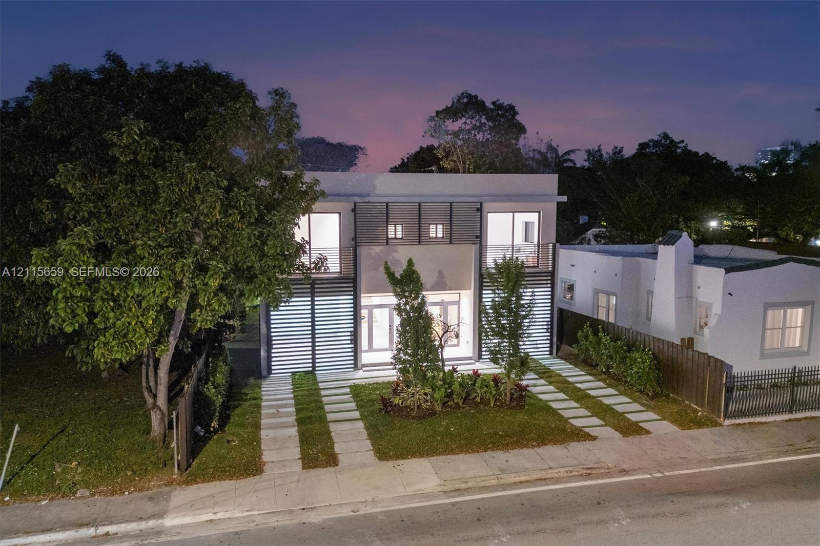 Modern two-story architectural exterior featuring smooth stucco finish, horizontal slat screening, and expansive glass entry doors