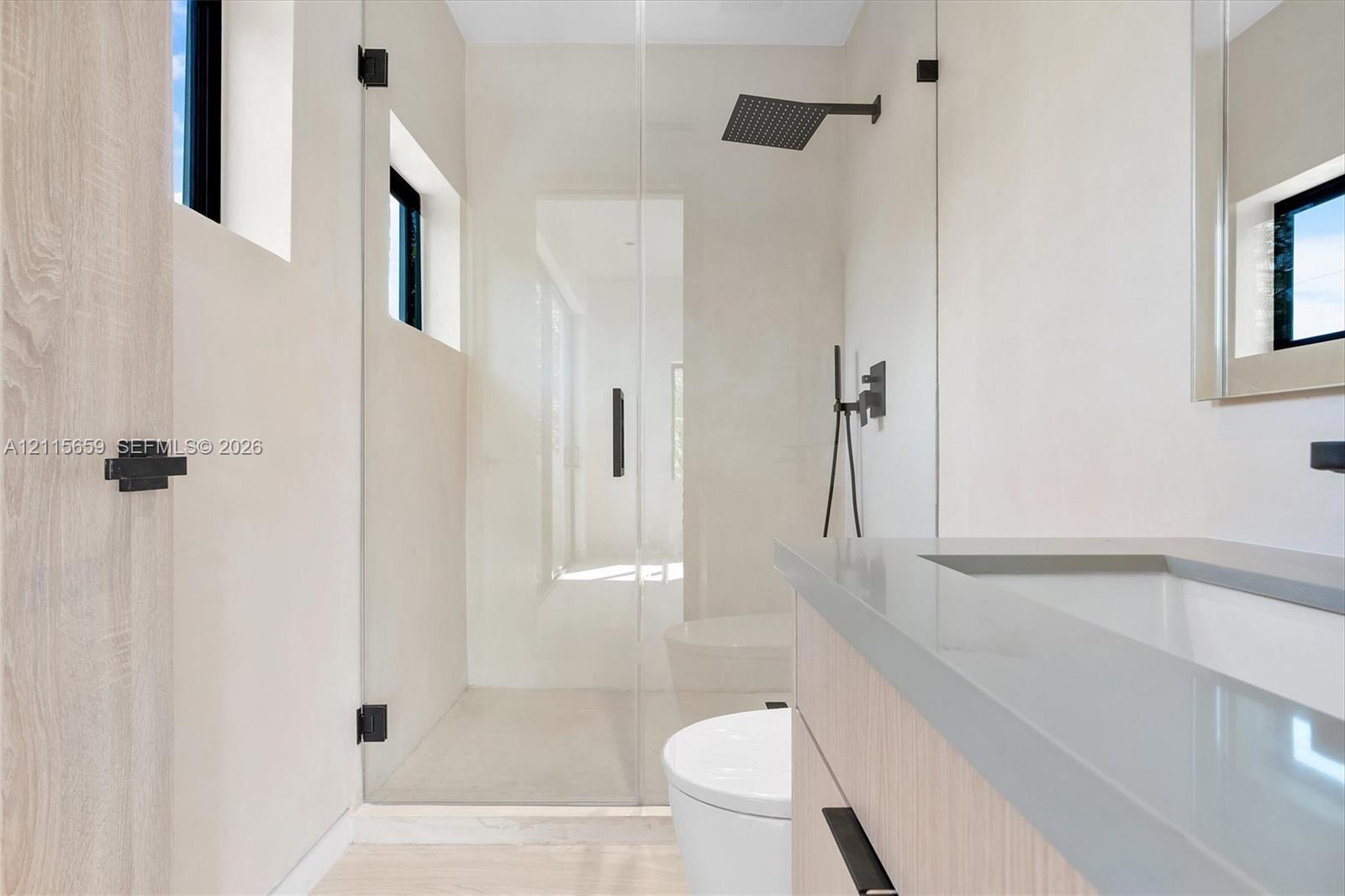 Bathroom featuring a wood-finish vanity with a stone countertop, a glass-enclosed walk-in shower with matte black rainfall showerhead, and high-contrast matte black hardware