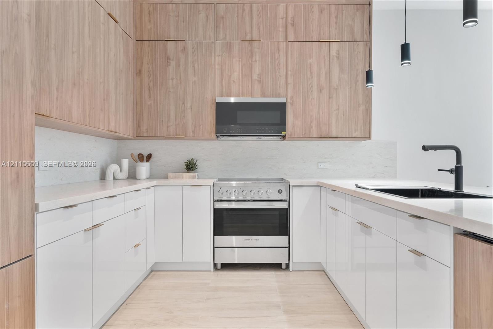 Kitchen featuring floor-to-ceiling wood-finish cabinetry, gloss white lower cabinetry, light-toned stone-finish countertops, stainless steel gas range with overhead microwave, and matte black plumbing fixtures