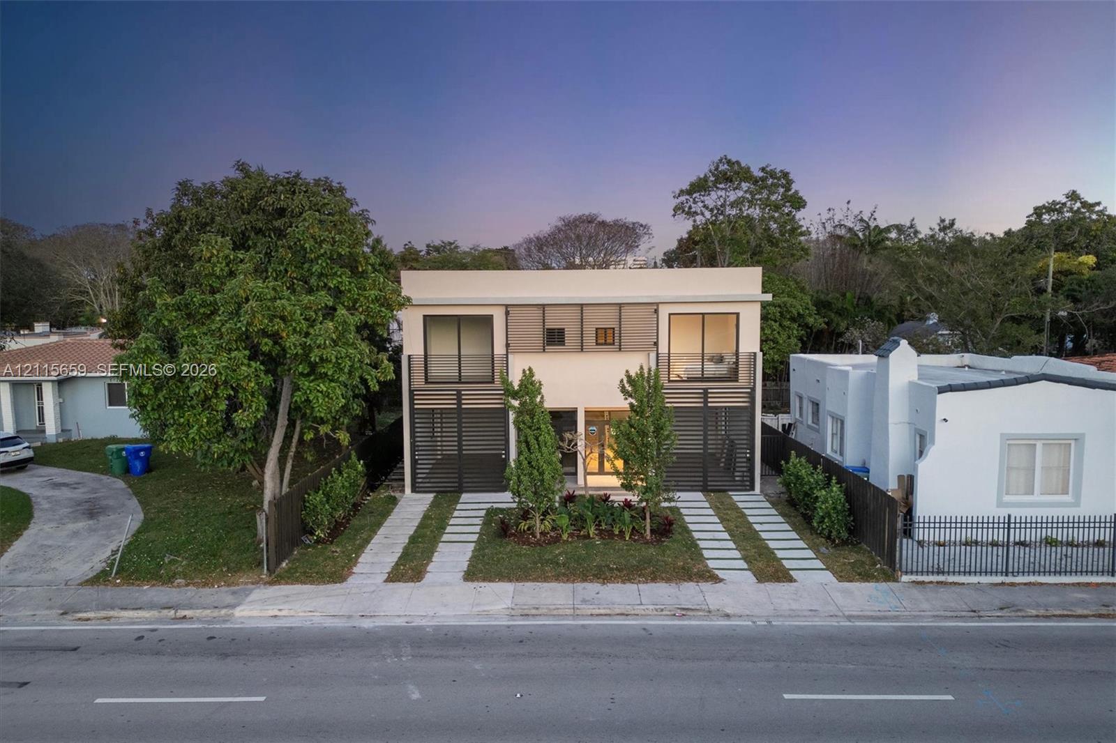 Two-story modern architectural exterior featuring a smooth stucco facade, black metal privacy screening, sliding glass balcony doors, and dual concrete paver driveways