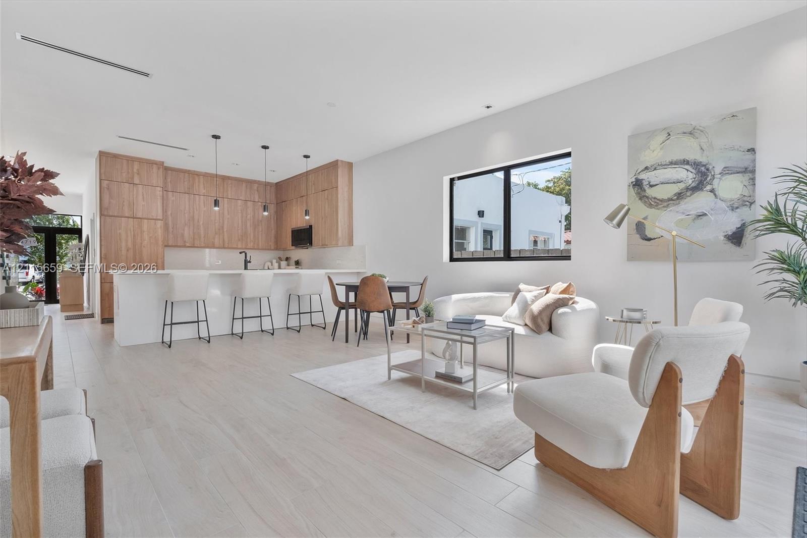 Open-concept living space featuring wood-finish cabinetry, a large kitchen island with quartz-surface countertops, light-toned wood-finish flooring, and recessed ceiling lighting