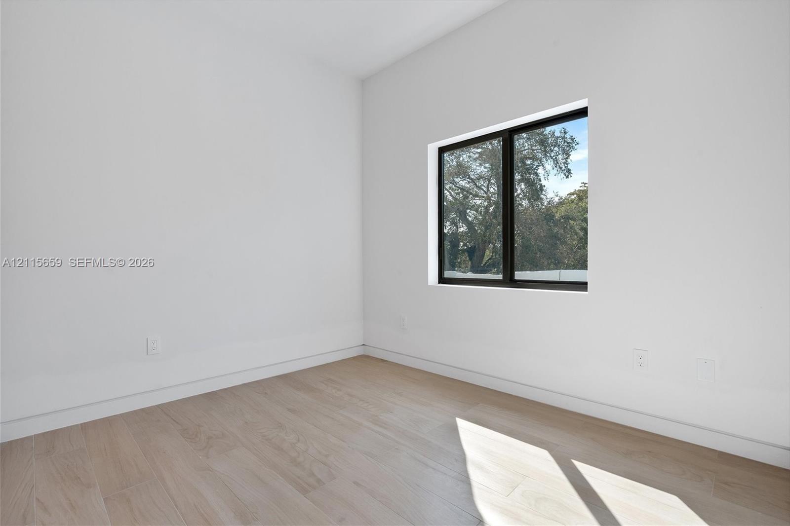 Interior space featuring neutral wall tones, wood-finish flooring, and a black-framed window