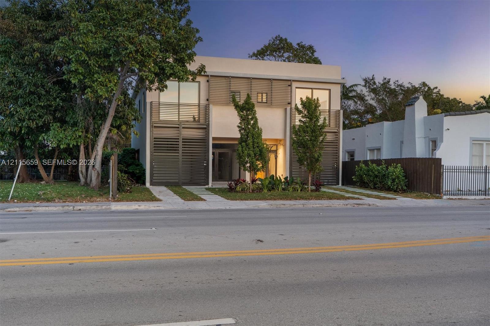 Contemporary two-story exterior featuring a smooth stucco facade, floor-to-ceiling glass doors, decorative metal screening, and upper-level balconies