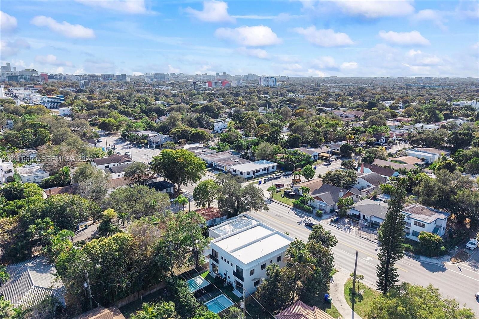 Aerial perspective of a two-story residence featuring a flat roof, white exterior, integrated swimming pool, and mature perimeter landscaping
