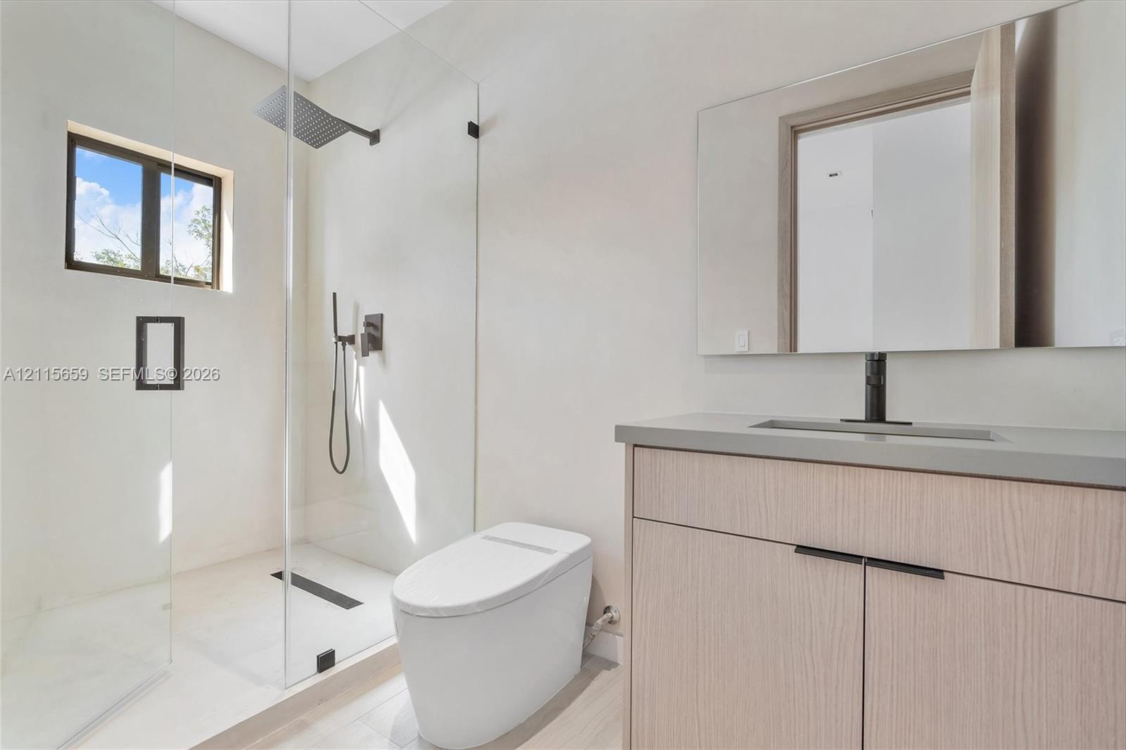 Modern bathroom featuring a wood-finish vanity, solid-surface countertop, frameless glass-enclosed shower, wall-mounted matte black fixtures, and a sleek rectangular mirror