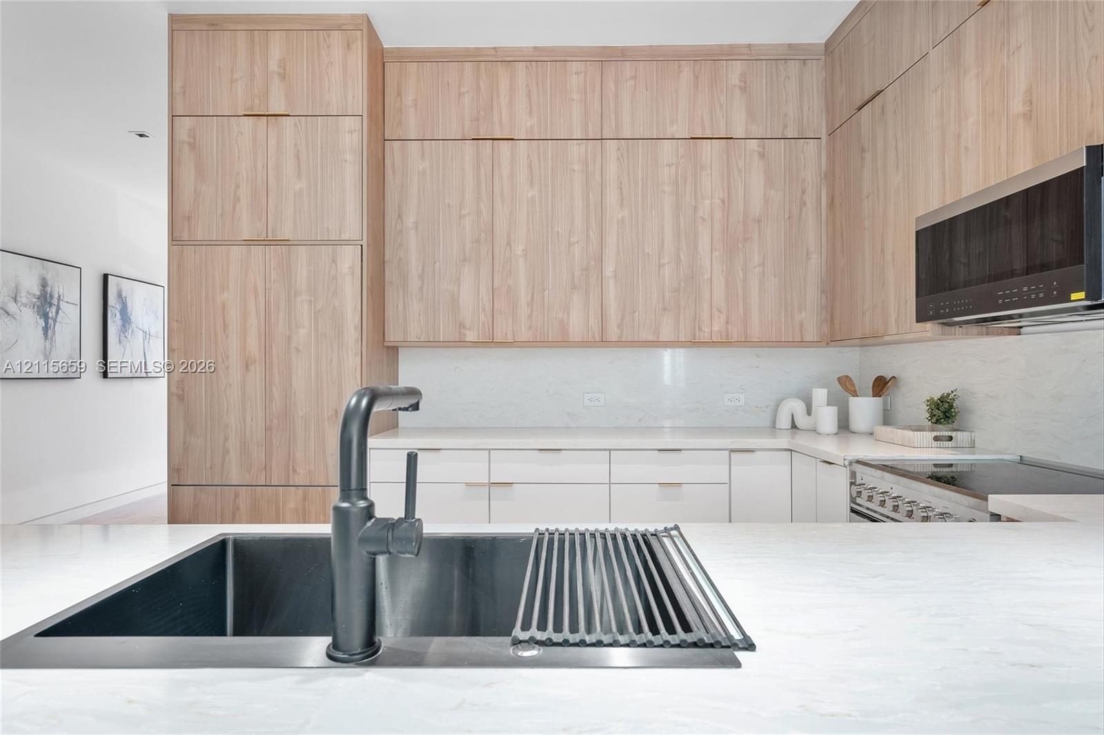 Kitchen featuring floor-to-ceiling wood-finish cabinetry, white stone-finish countertops, matte black single-handle faucet, integrated stainless steel sink, and stainless steel microwave