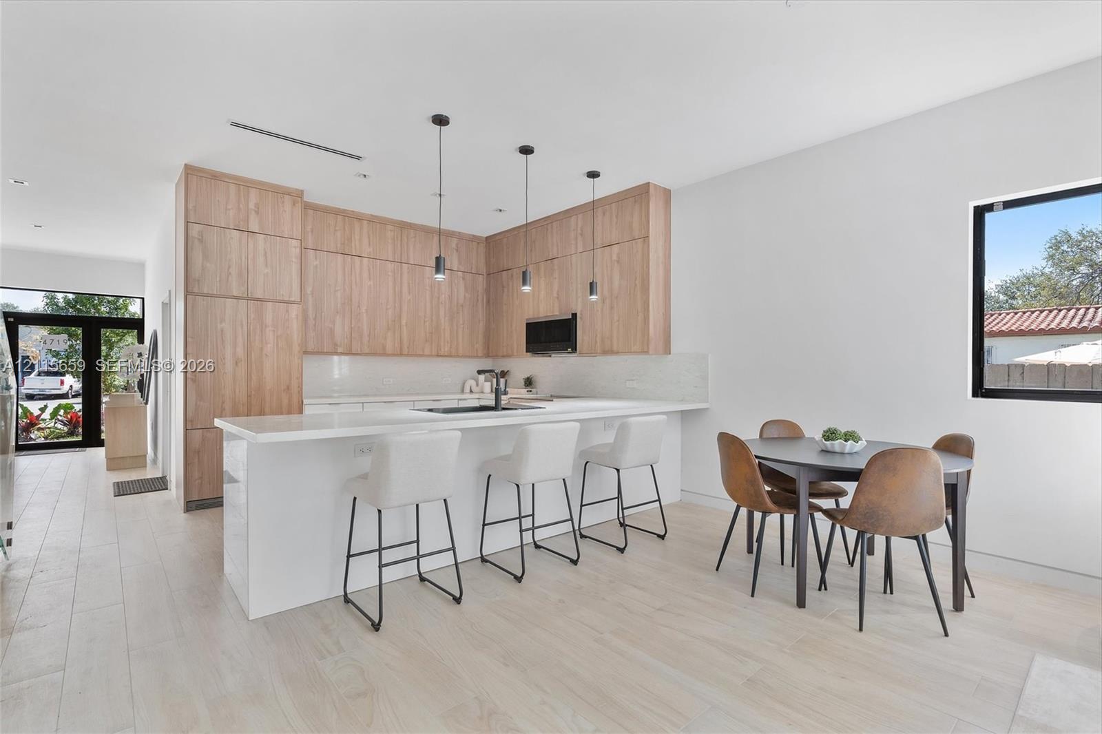 Modern kitchen featuring wood-finish cabinetry, a white countertop island, integrated lighting pendants, and light-toned tile flooring