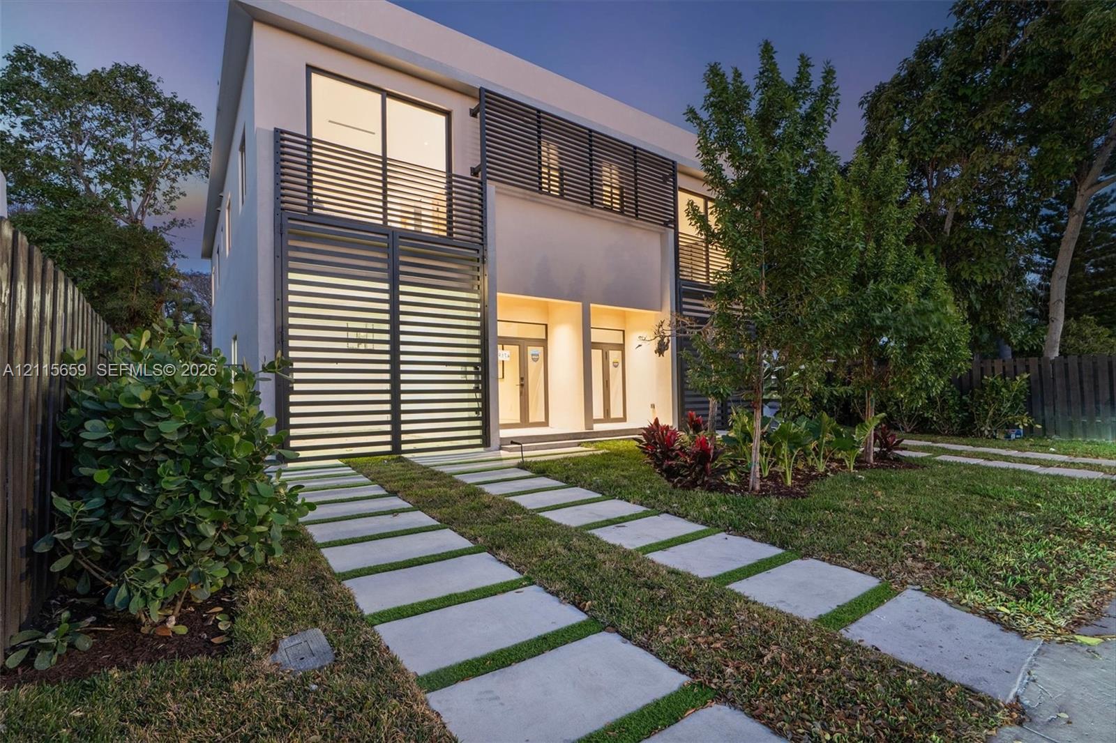 Contemporary two-story exterior featuring a smooth stucco finish, horizontal metal louvered privacy screening, glass sliding doors, and a linear paver driveway