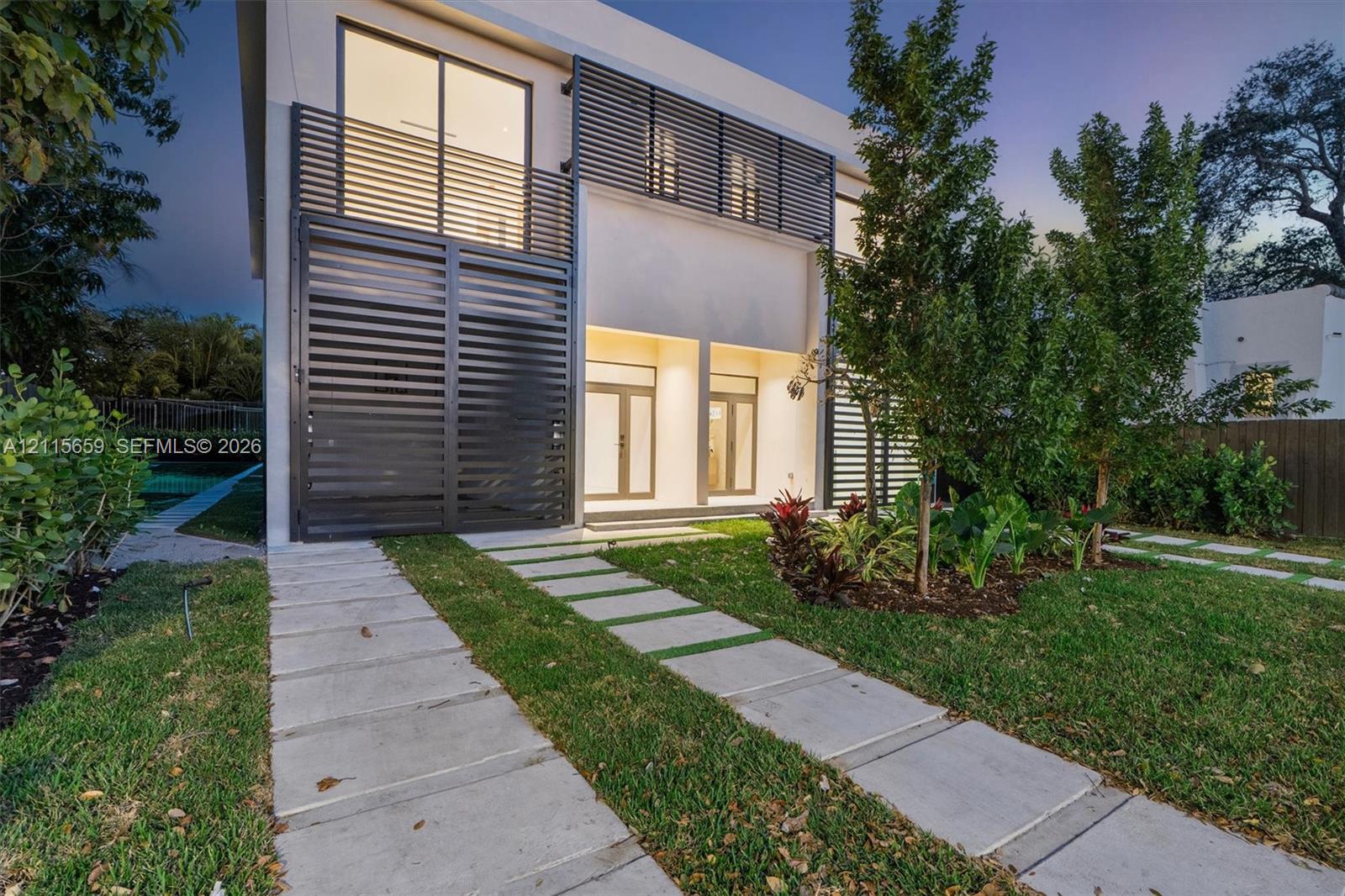 Modern two-story architectural exterior featuring smooth stucco finish, black metal privacy screens, large-format glass slider doors, and concrete paver walkway