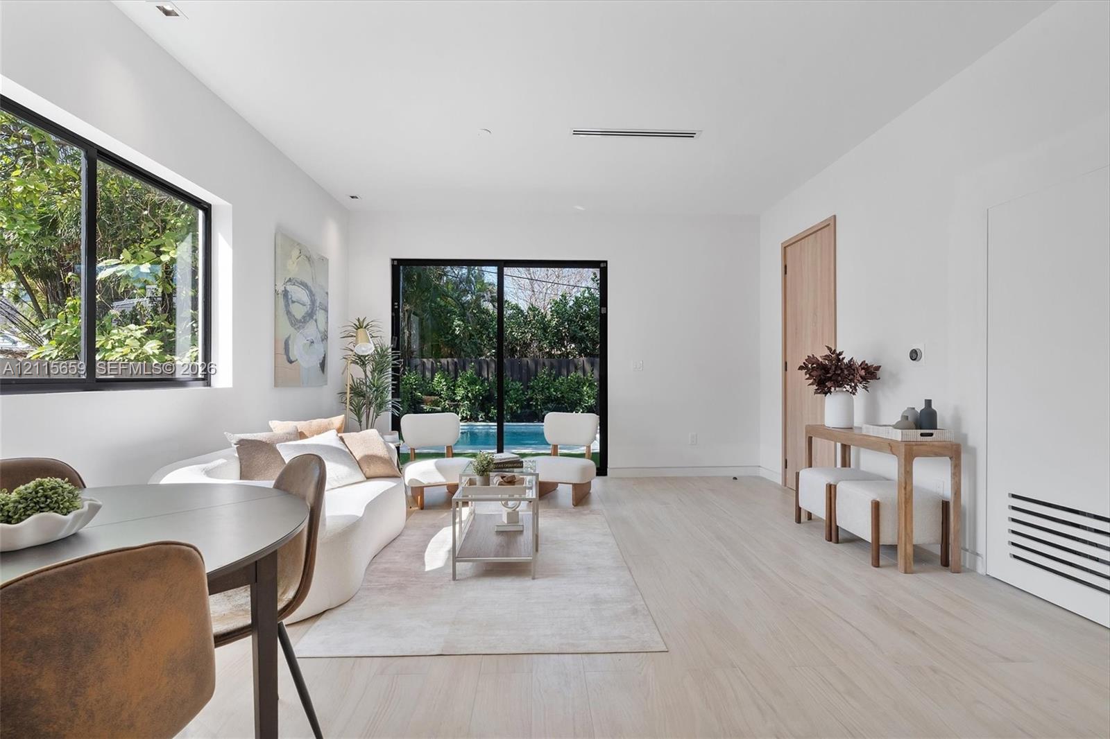 Open-concept interior featuring light wood-finish flooring, recessed lighting, expansive black-framed windows, and sliding glass doors with exterior pool access