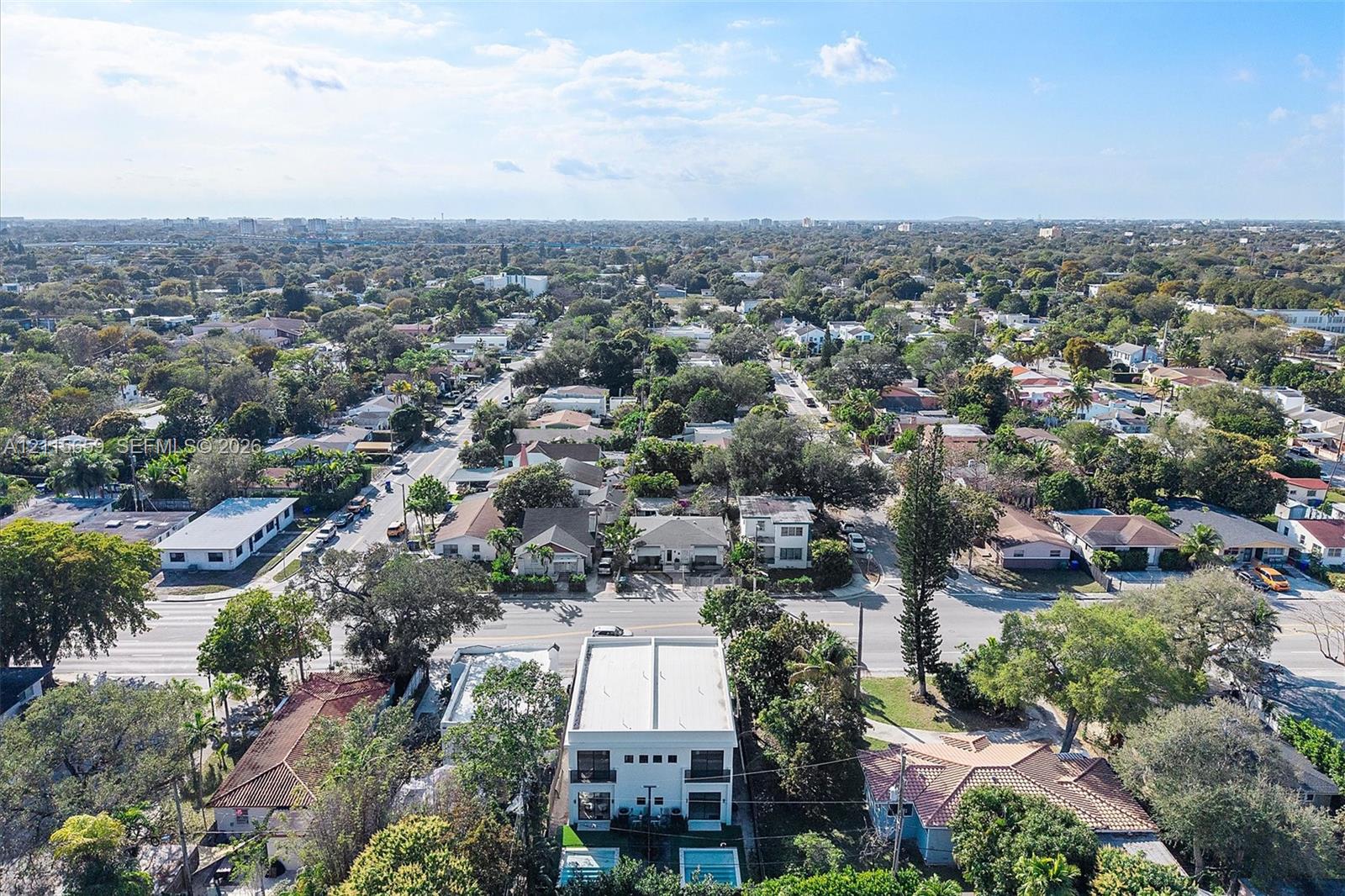Aerial perspective of a multi-story residence featuring a flat roofline, two levels of balcony structures, a ground-level rectangular swimming pool, and established surrounding canopy trees