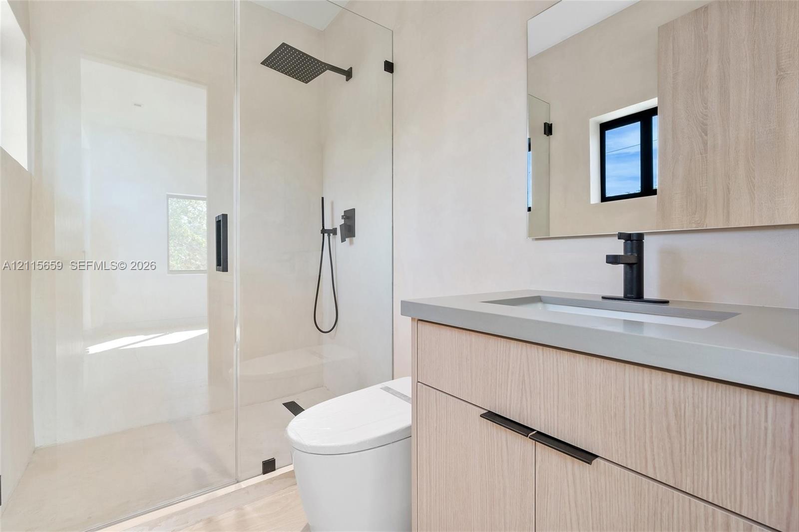 Bathroom featuring a wood-finish vanity with a stone countertop, a glass-enclosed shower with a rainfall showerhead, a wall-mounted mirror, and matte black fixtures