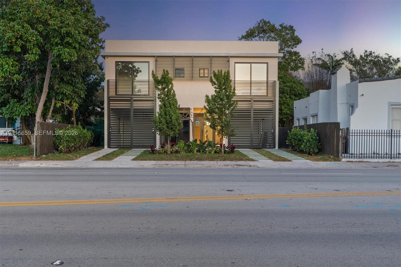 Contemporary two-story exterior featuring a smooth stucco finish, vertical metal louvers, expansive floor-to-ceiling glass panels, and dual concrete paved driveways