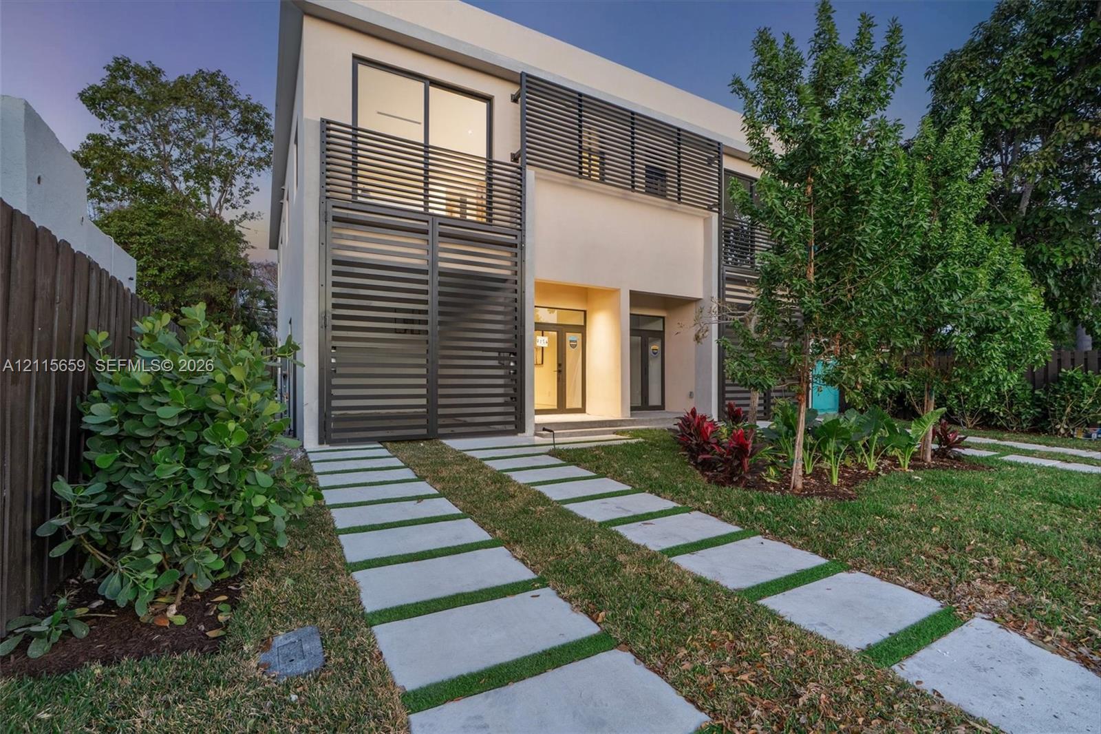 Modern two-story residence featuring a smooth stucco exterior, horizontal metal privacy screening, integrated balcony, and a permeable paver driveway system