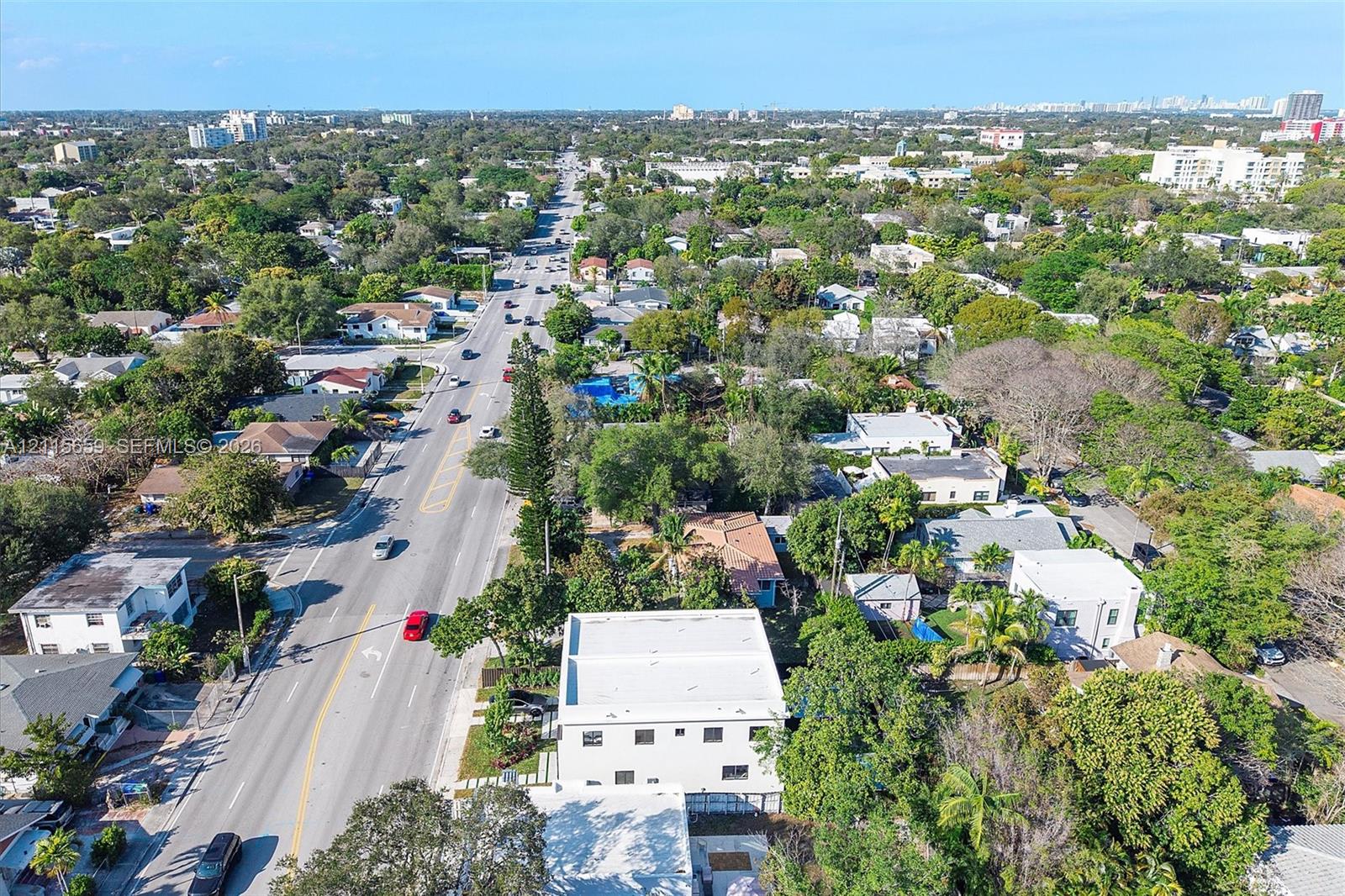 Aerial perspective of a multi-story structure featuring a flat roof and concrete-finish exterior, situated on a lot with established canopy trees and paved access