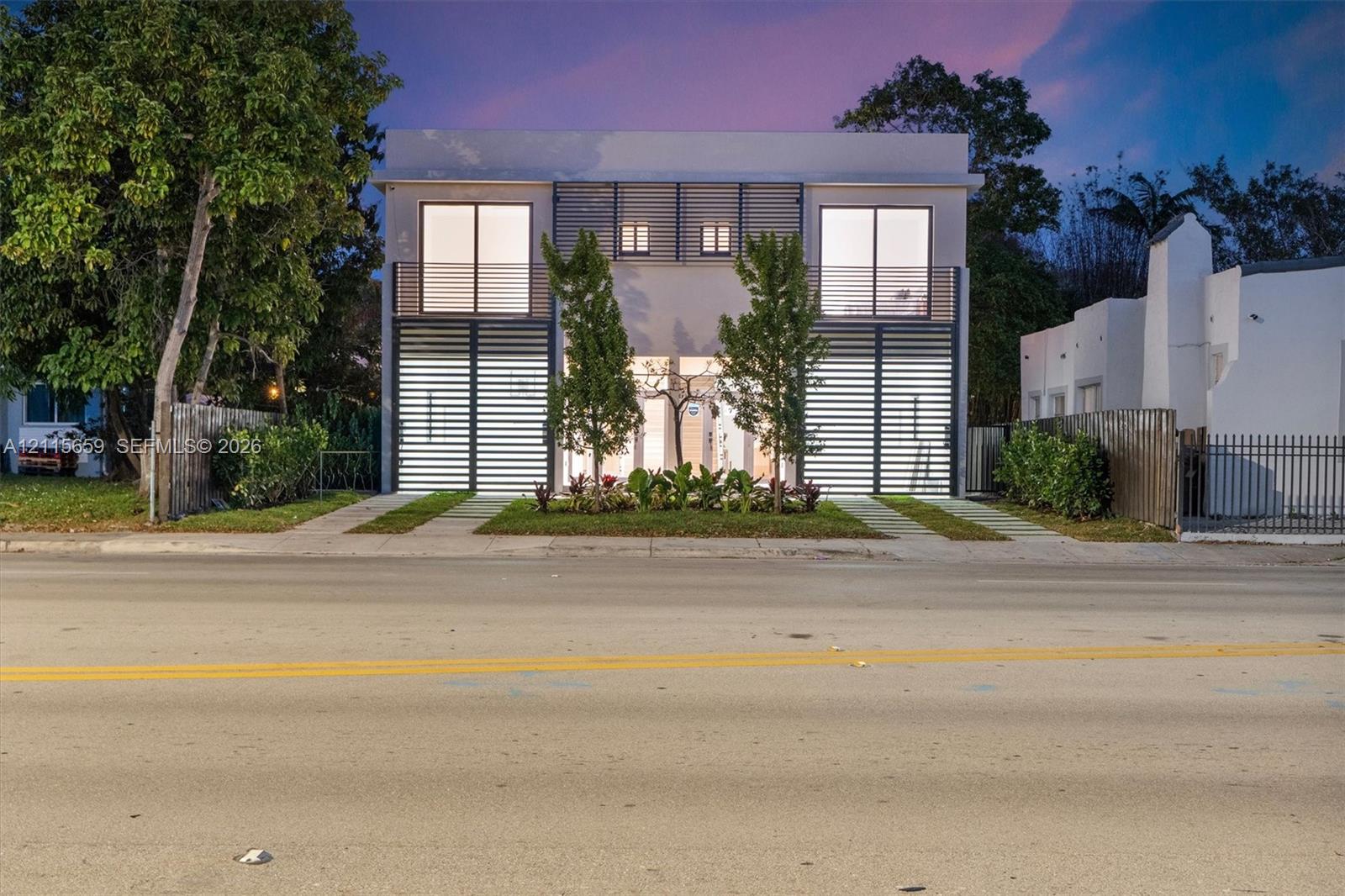Two-story contemporary exterior featuring horizontal slat privacy screening, dual upper-level balconies, smooth stucco finish, and manicured landscaping