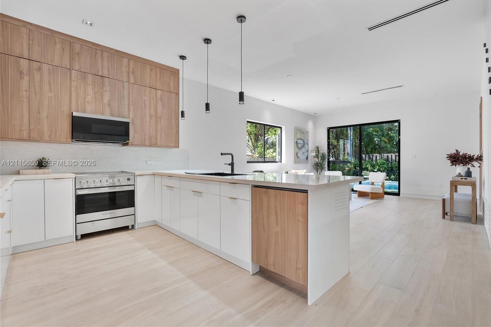 Kitchen featuring two-tone wood-finish and matte white cabinetry, stone-surfaced island, stainless steel range with overhead microwave, and wood-finish flooring