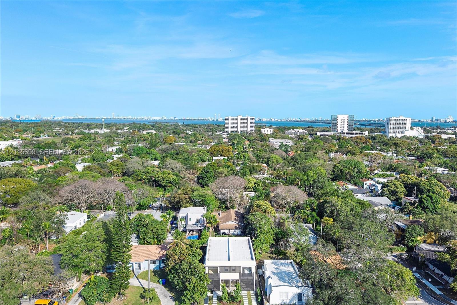 Aerial perspective of a multi-level residence featuring a flat roofline, paved driveway, and mature landscaping within a tree-lined residential area