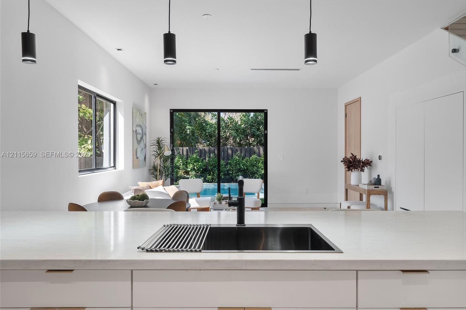 Kitchen featuring a stone-surface island, undermount stainless steel sink, matte black faucet, and three modern pendant lights