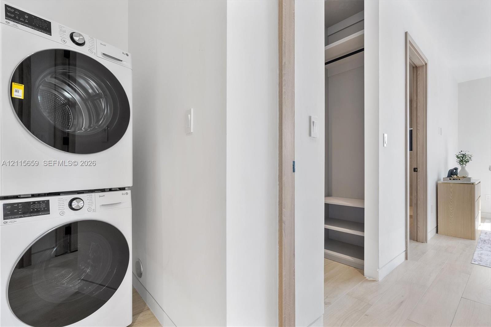 Stacked front-loading washer and dryer, built-in shelving, and light-toned wood-finish flooring