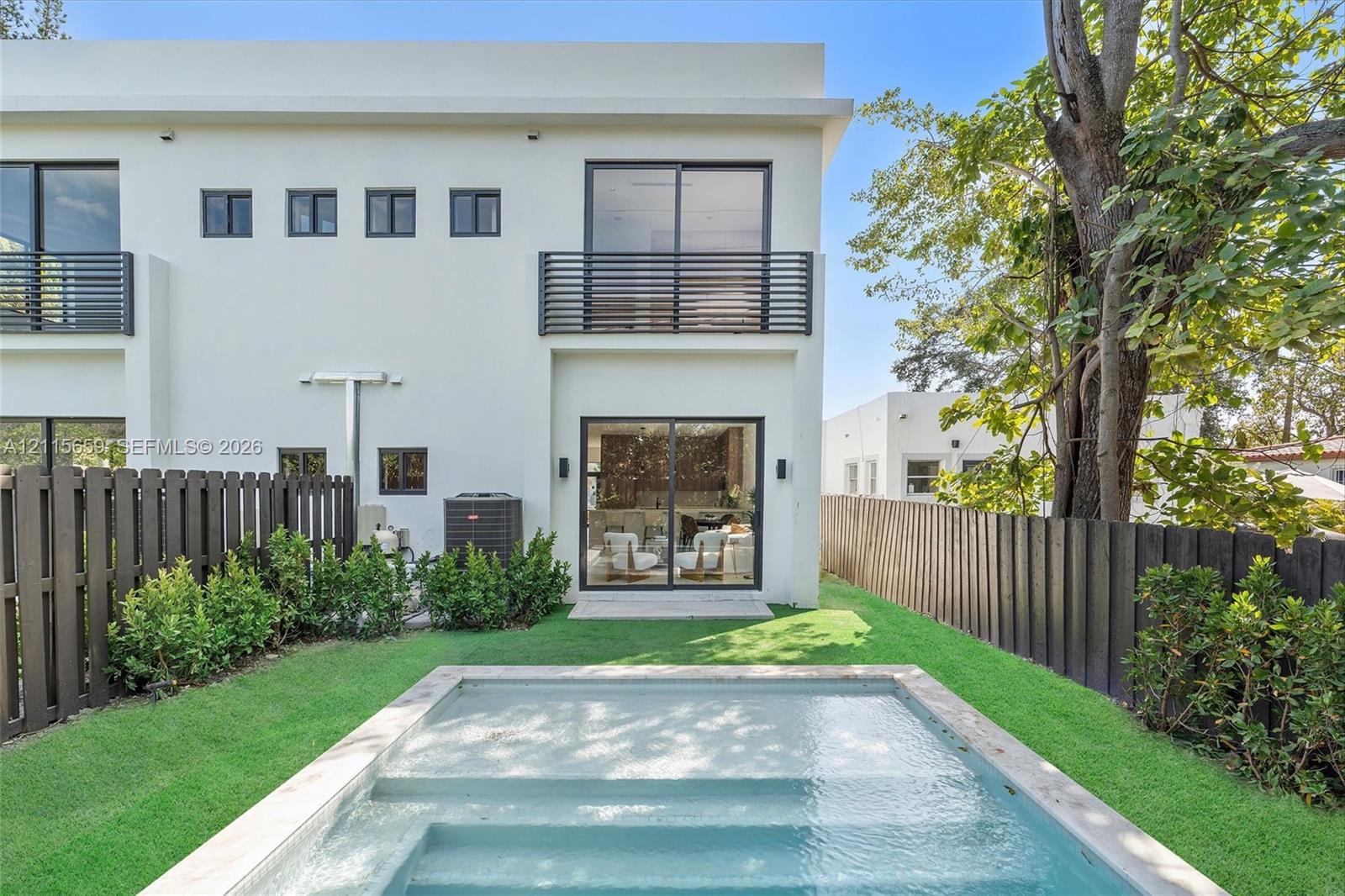 Contemporary two-story exterior featuring smooth stucco finish, black horizontal balcony railings, sliding glass doors, a rectangular swimming pool, and wood-style privacy fencing