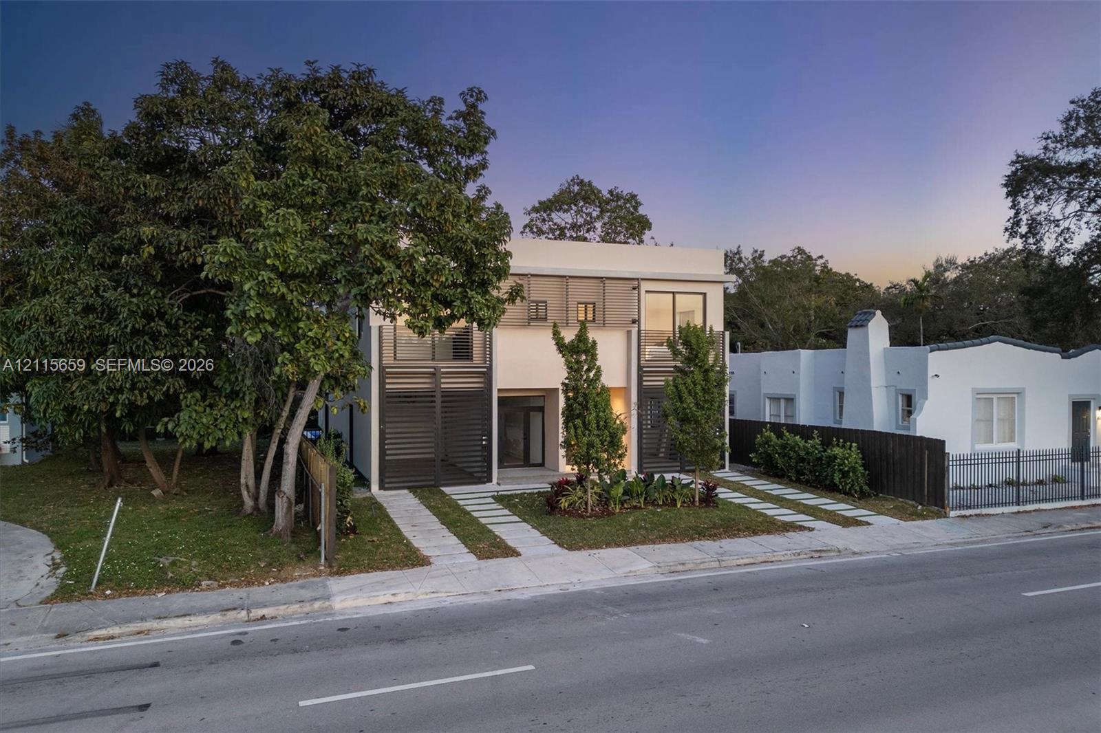 Modern two-story exterior featuring a smooth stucco finish, dark metal louvered privacy screens, expansive glass sliding doors, multiple balconies, and a concrete paver driveway