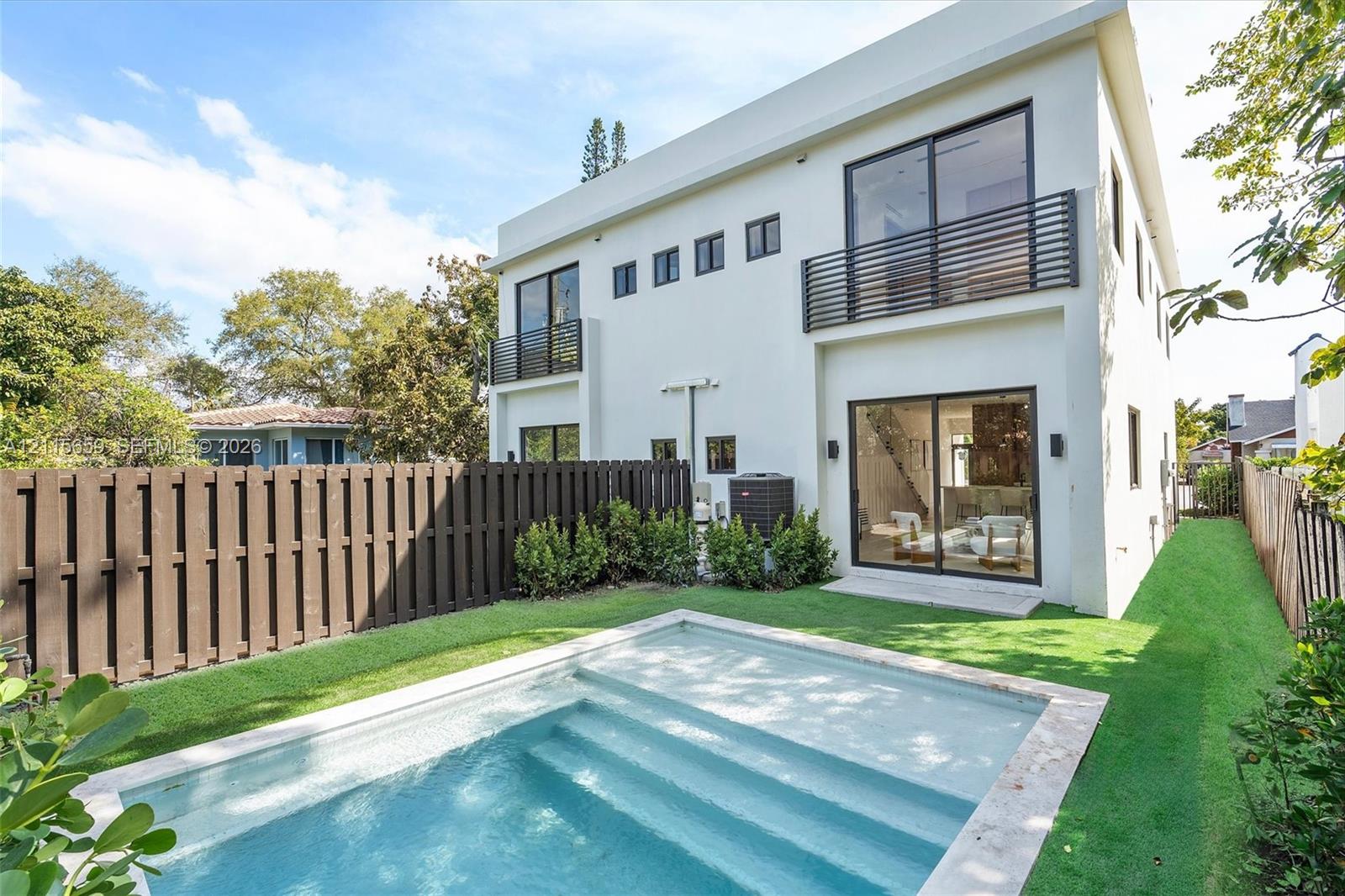 Modern two-story exterior featuring a private swimming pool with built-in steps, second-floor balconies with horizontal railings, sliding glass doors, and a wood-slat privacy fence