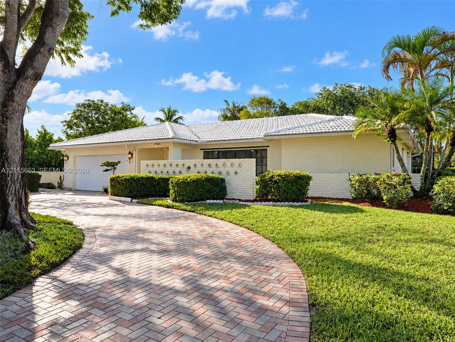Single-story residence featuring painted brick masonry, a white tile roof, a curved herringbone-patterned brick paver driveway, and integrated decorative screen wall accents