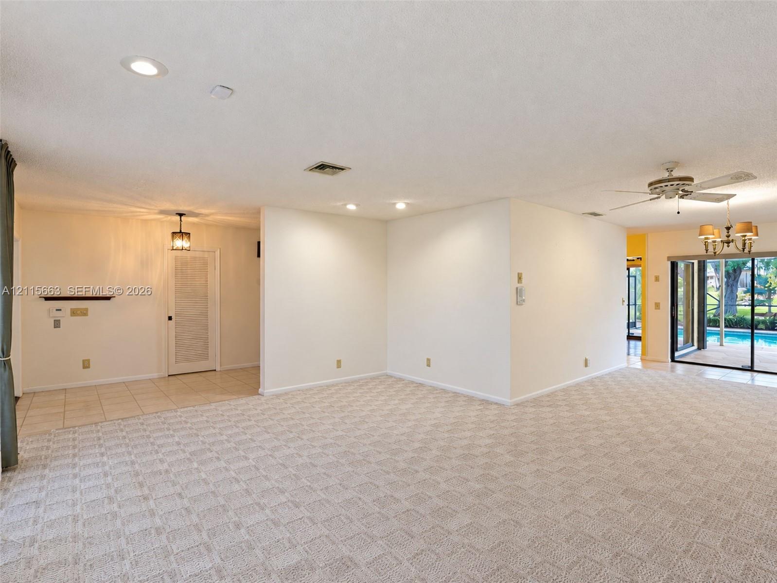 Neutral-toned carpeting, recessed lighting, multi-arm chandelier, ceiling fan, and sliding glass doors