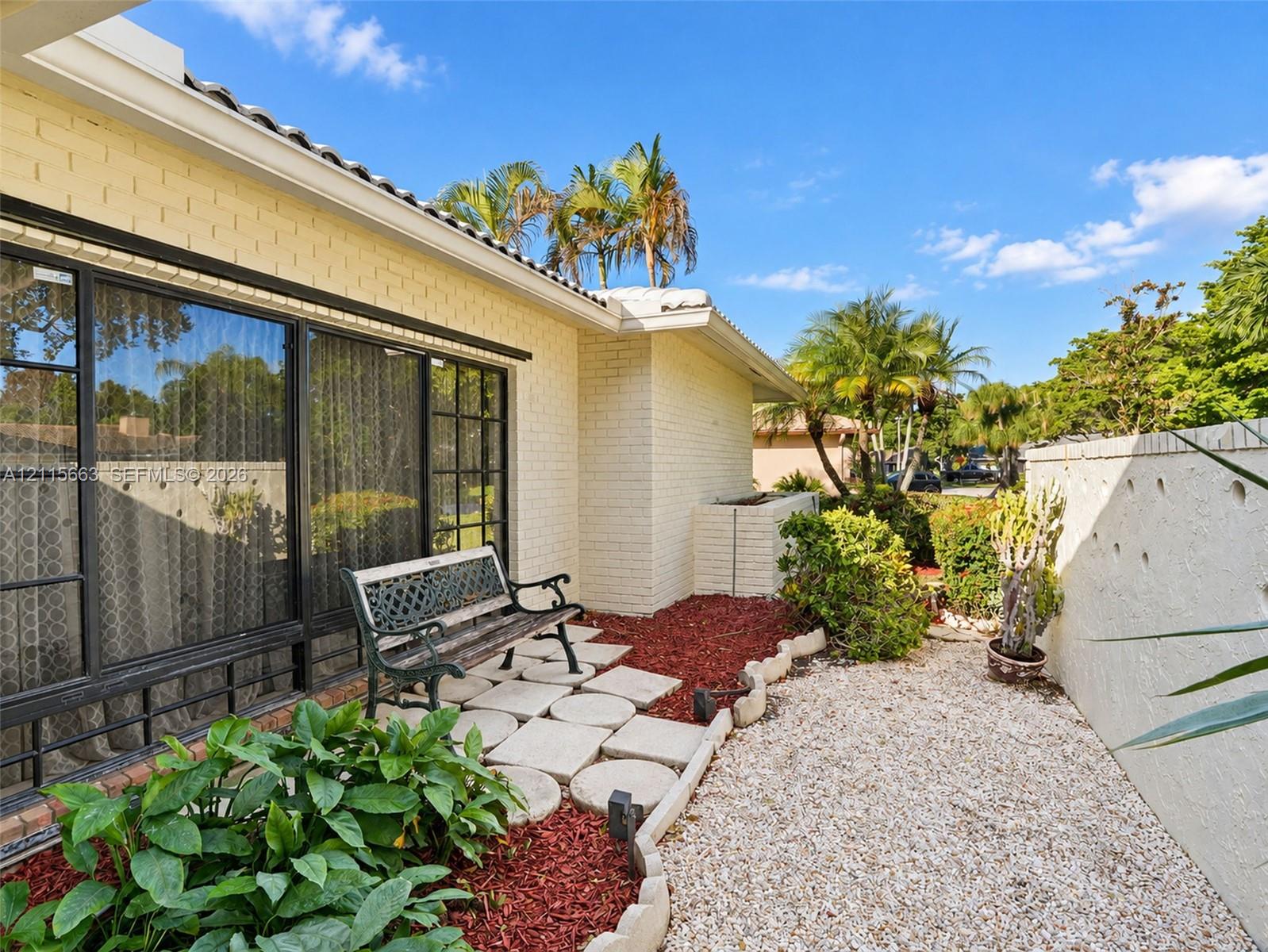 Light-colored brick exterior featuring large-pane metal windows, concrete paver pathway, decorative landscape edging, and low-maintenance gravel ground cover