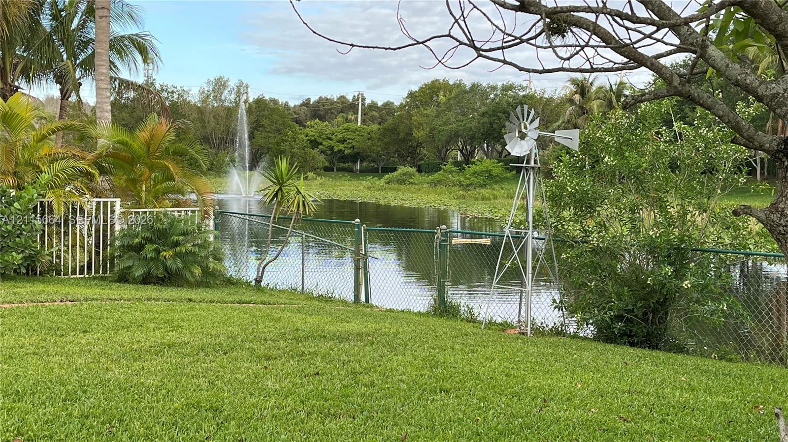 Waterfront backyard featuring a tiered lawn, decorative metal windmill, water fountain, and chain-link perimeter fencing
