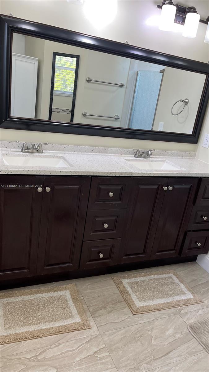 Double vanity featuring dark wood cabinetry, solid-surface countertops with dual undermount sinks, a full-width framed mirror, and tiled flooring