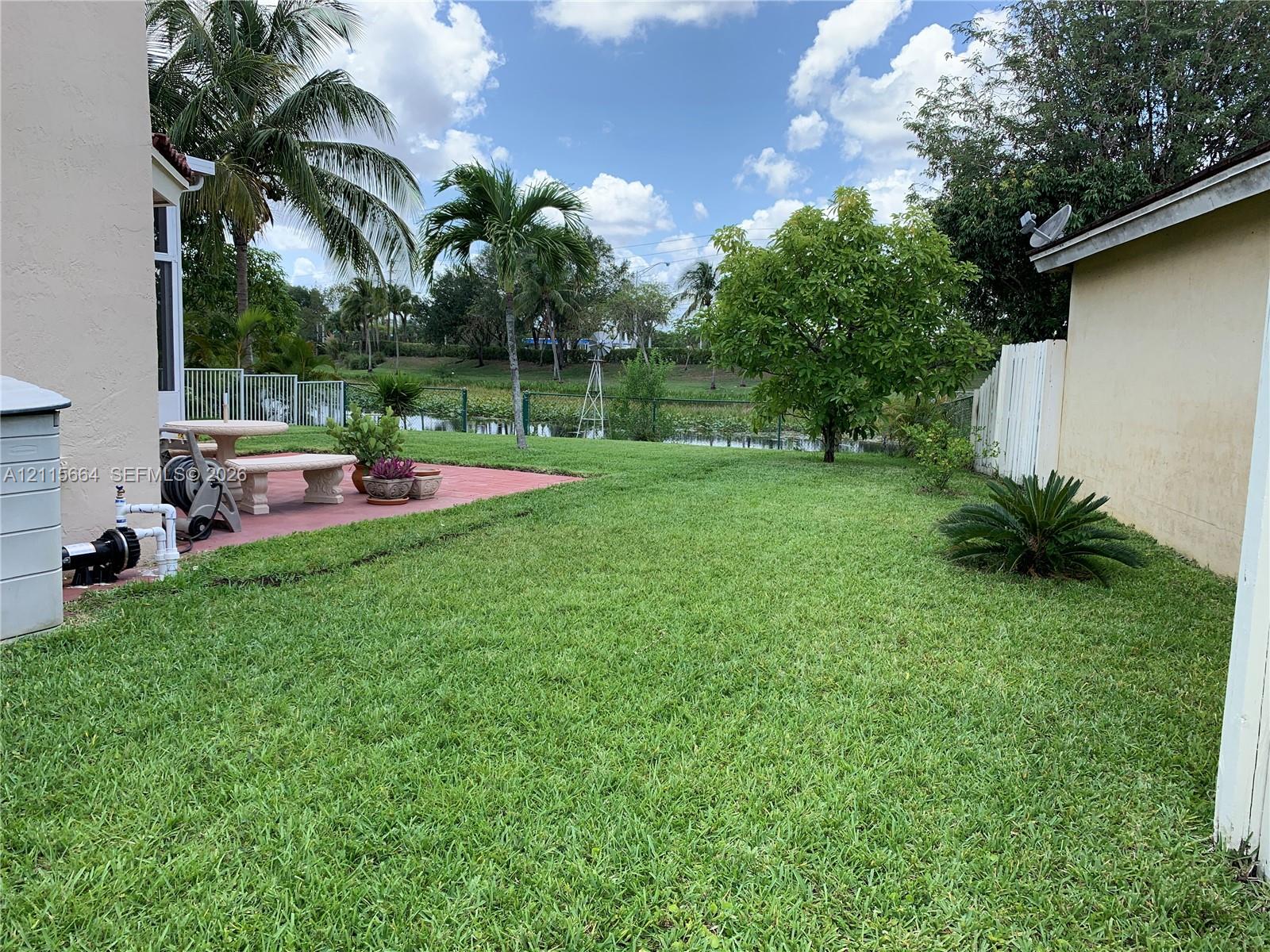 Backyard featuring a paved patio, expansive lawn, mature tropical landscaping, and water frontage