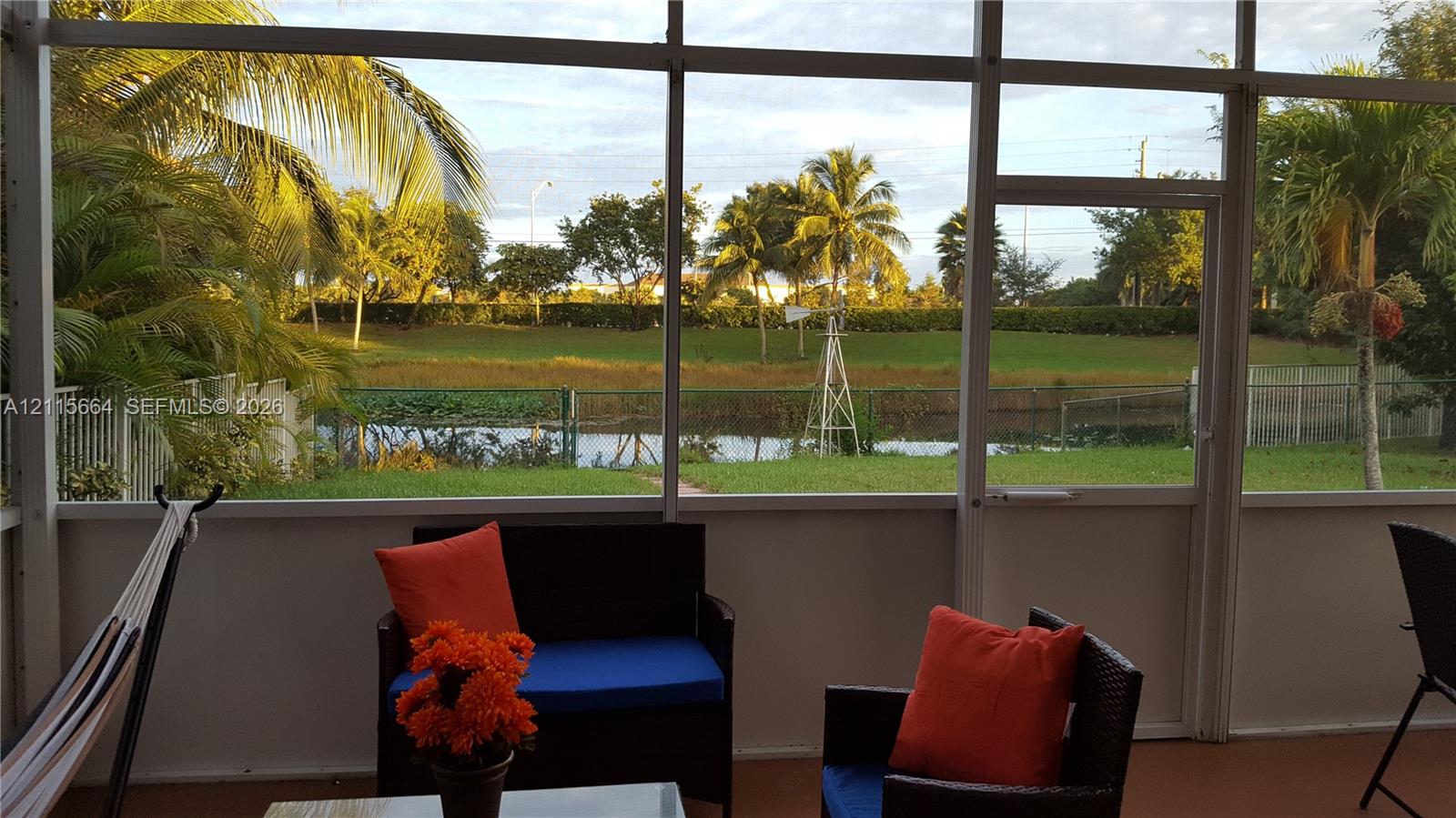 Screened-in enclosure featuring a concrete floor, metal framing, and a backdrop of a water feature, manicured landscaping, and mature palm trees