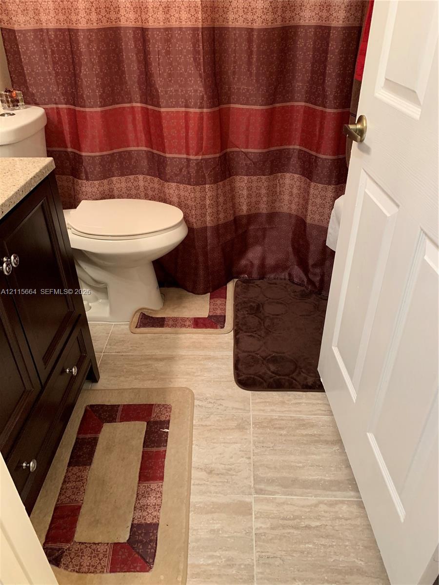Dark-finish cabinetry featuring a light-toned solid surface countertop, ceramic tile flooring, and a standard-height toilet