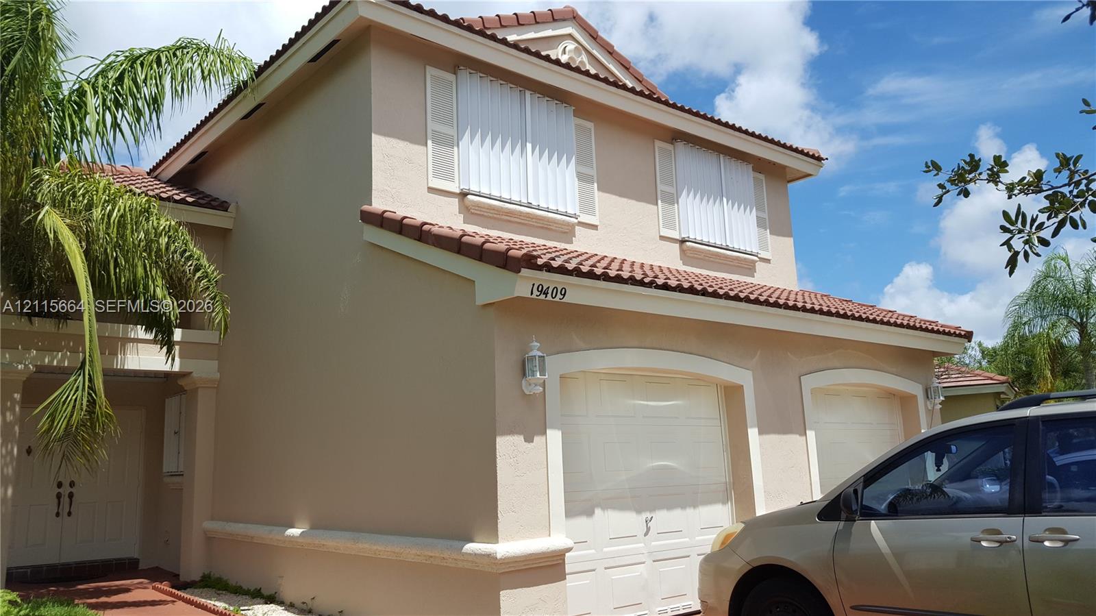 Two-story stucco exterior featuring a terra-cotta tile roof, a double-bay garage, and exterior shutters