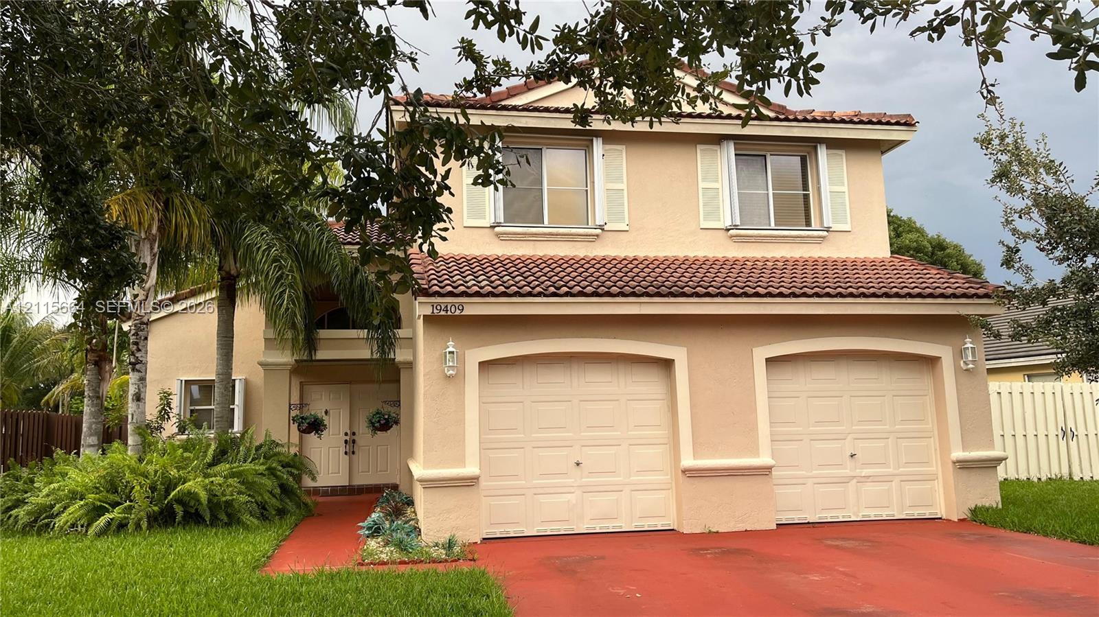 Two-story exterior featuring a textured stucco facade, a red tile roof, and a dual-car garage with arched entryways