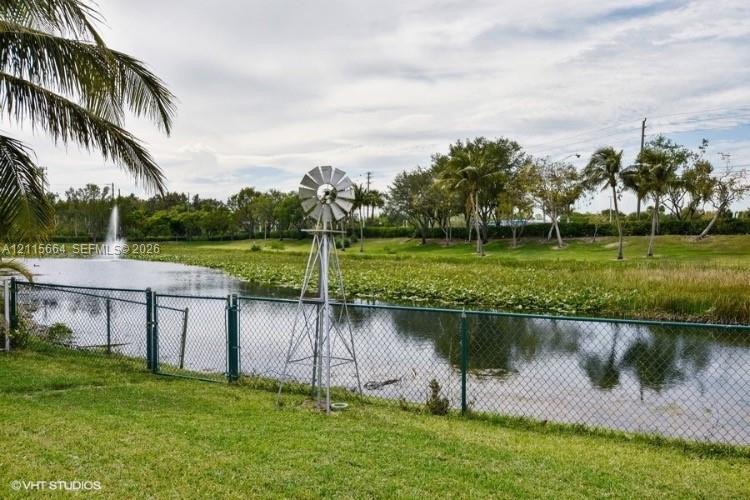 Waterfront parcel featuring a pond with a fountain, a metal windmill, palm trees, and perimeter chain-link fencing