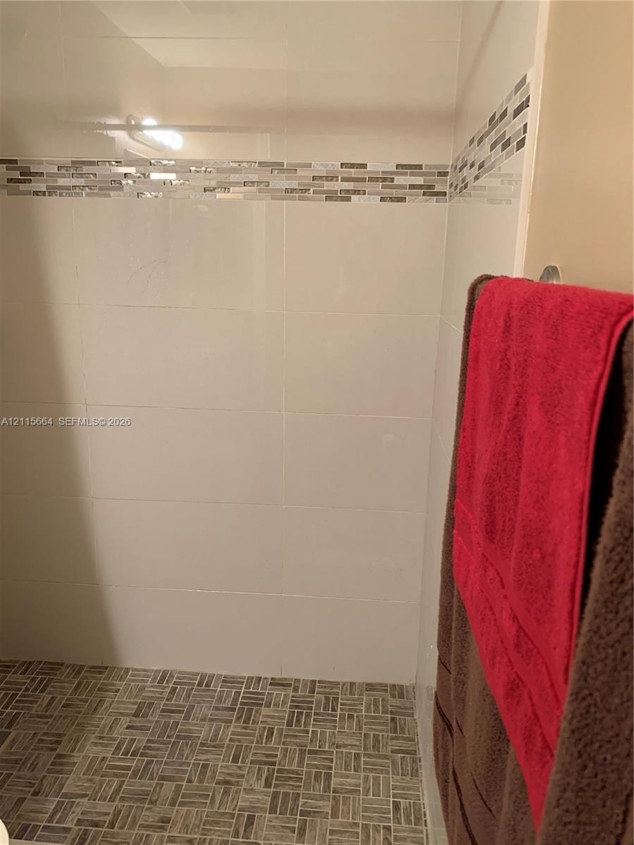 Shower stall featuring large-format white wall tile, a decorative glass-blend mosaic accent border, and a patterned tile floor