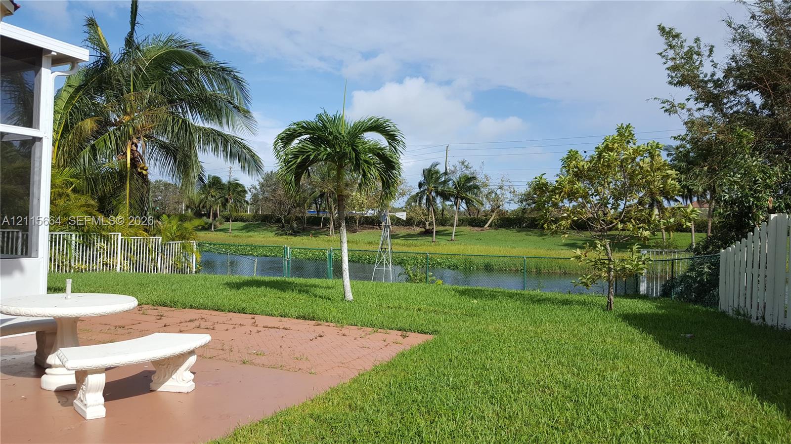 Backyard featuring a paved patio, manicured lawn, established palm trees, and direct waterfront access