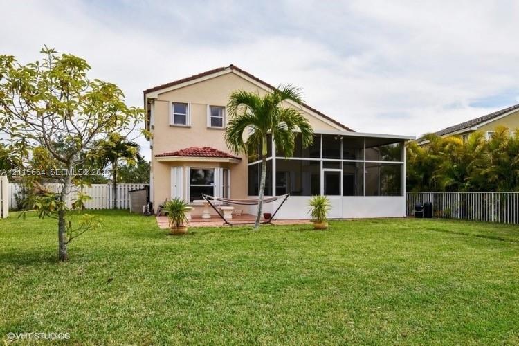 Stucco exterior residence featuring a screened-in lanai, tile roof, paved patio area, and fenced backyard
