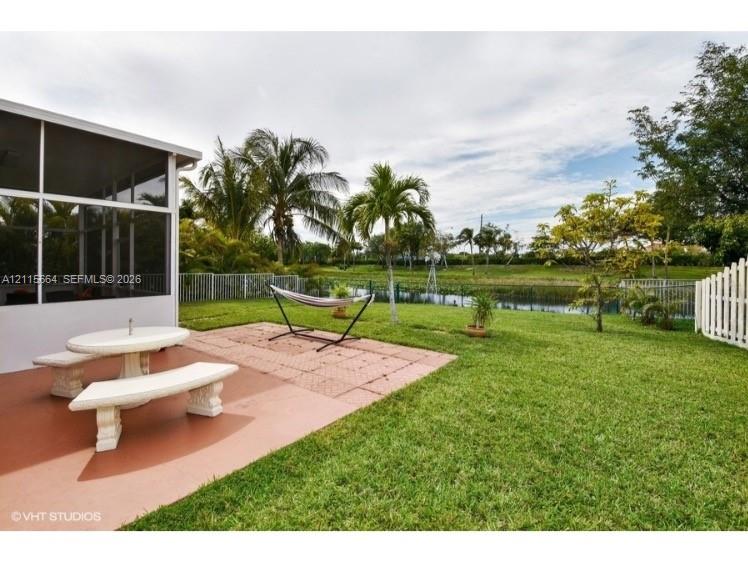 Screened-in outdoor living space with a concrete patio, landscaped lawn, metal perimeter fencing, and water frontage