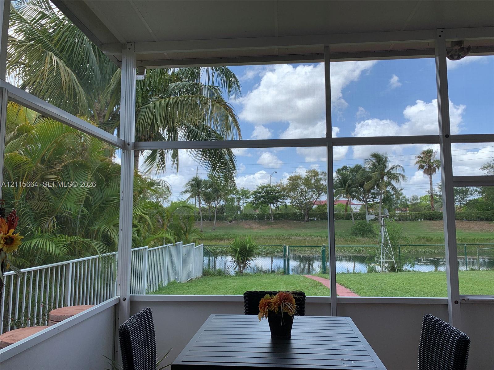 Screened-in patio featuring an aluminum frame, metal picket fencing, and direct exposure to a pond and mature landscaping